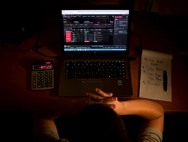 Игроман поздно ночью с ноутбуком и калькулятором проигрышей